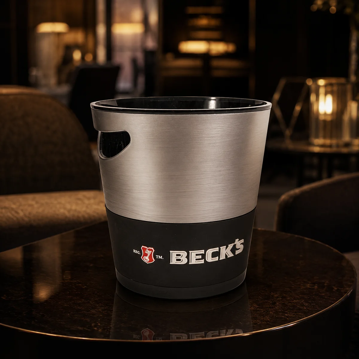 Acél és fekete jégvödör Beck's címkével, sötét pulton, városi fények előtt