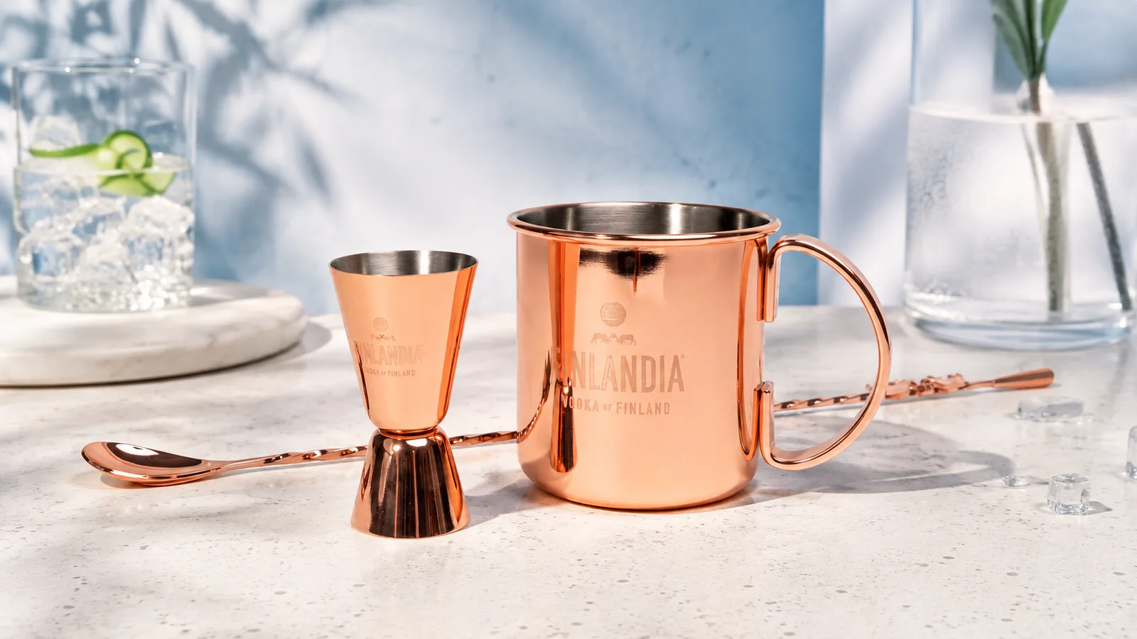 Réz Moscow Mule bögre Finlandia logóval, mellette adagoló és bárkanál, világos pulton