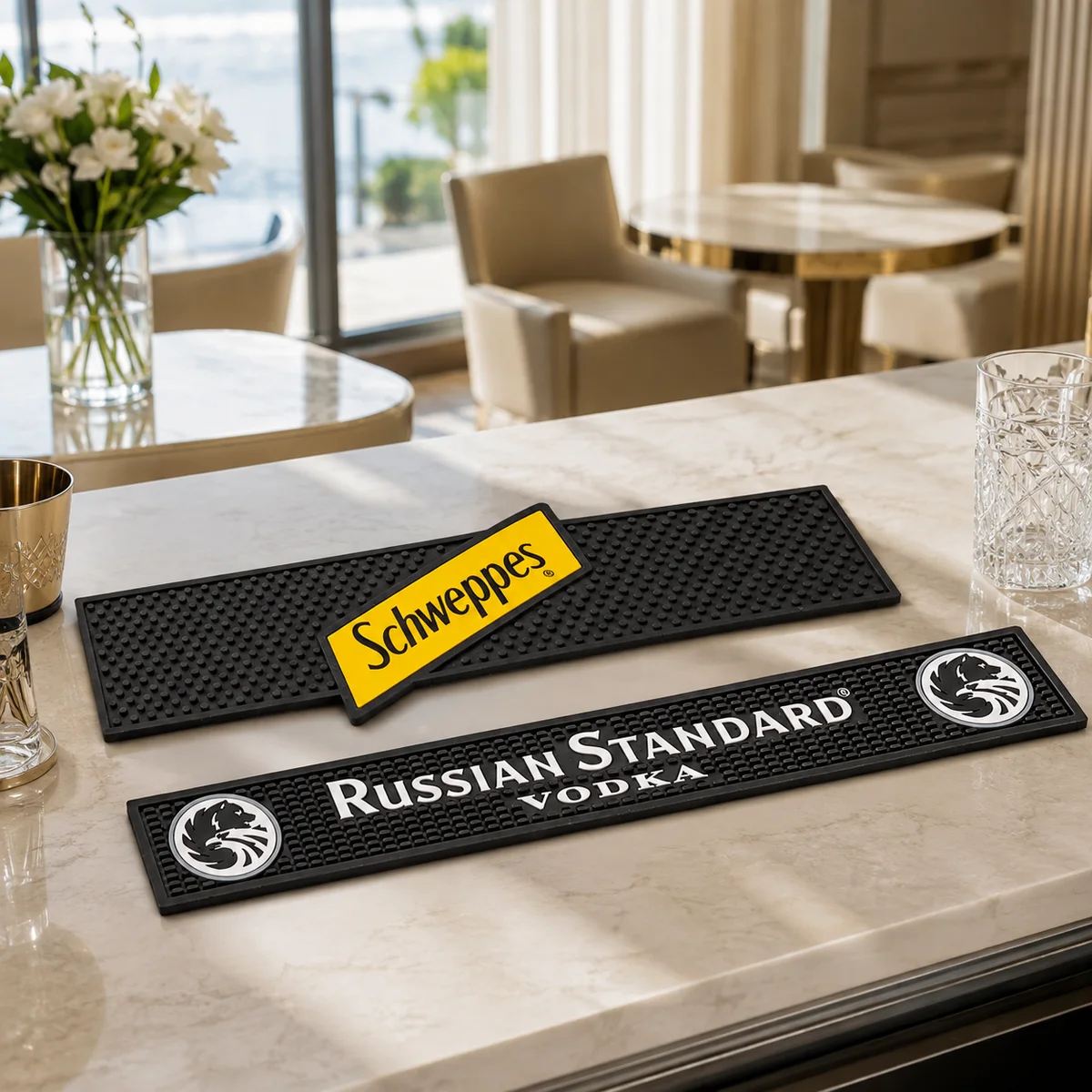 Két fekete gumi bárpult-alátét Schweppes és Russian Standard emblémával, világos pulton