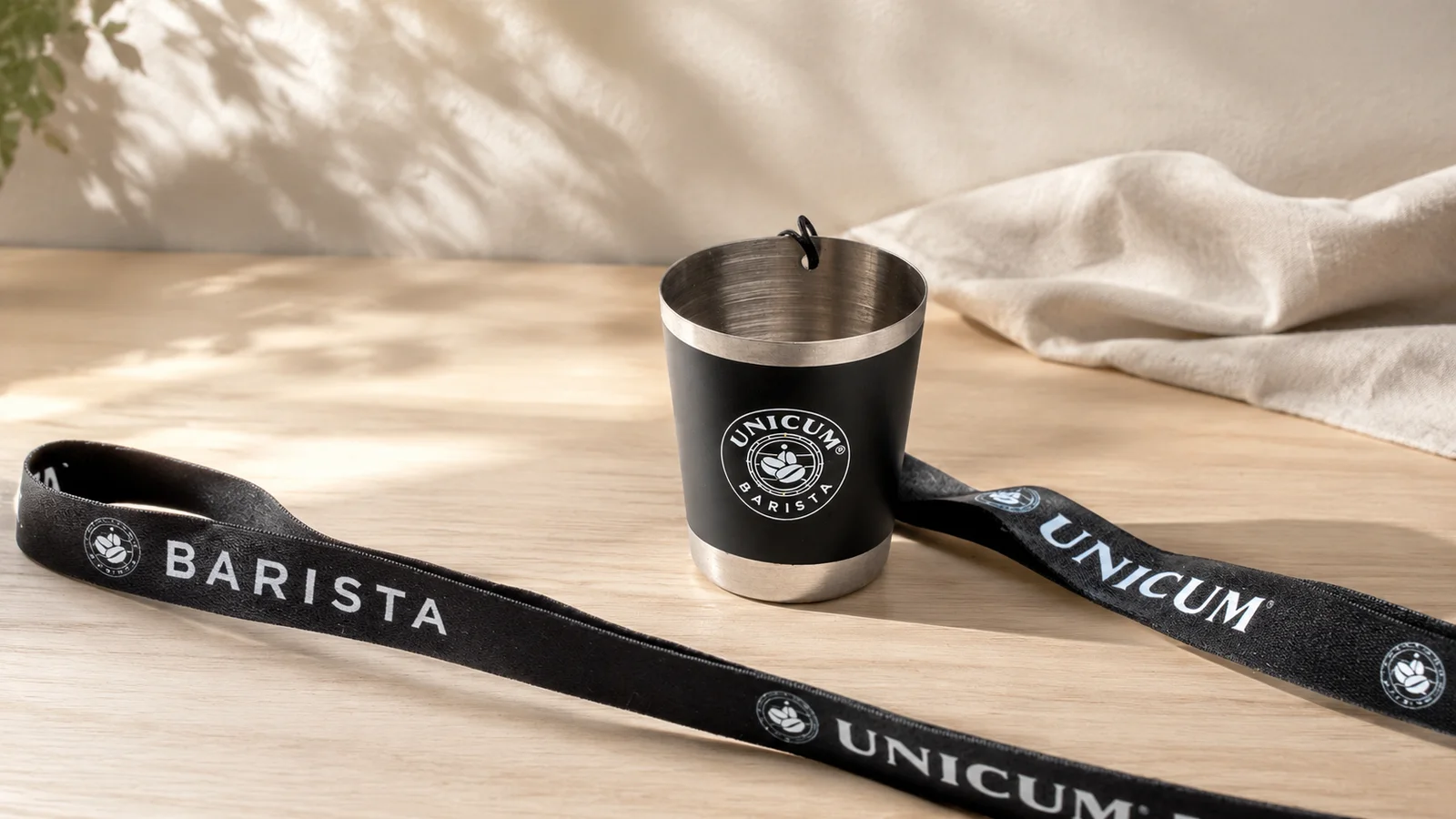 Fekete feles edény Unicum Barista emblémával, hosszú nyakpánttal, világos fapulton