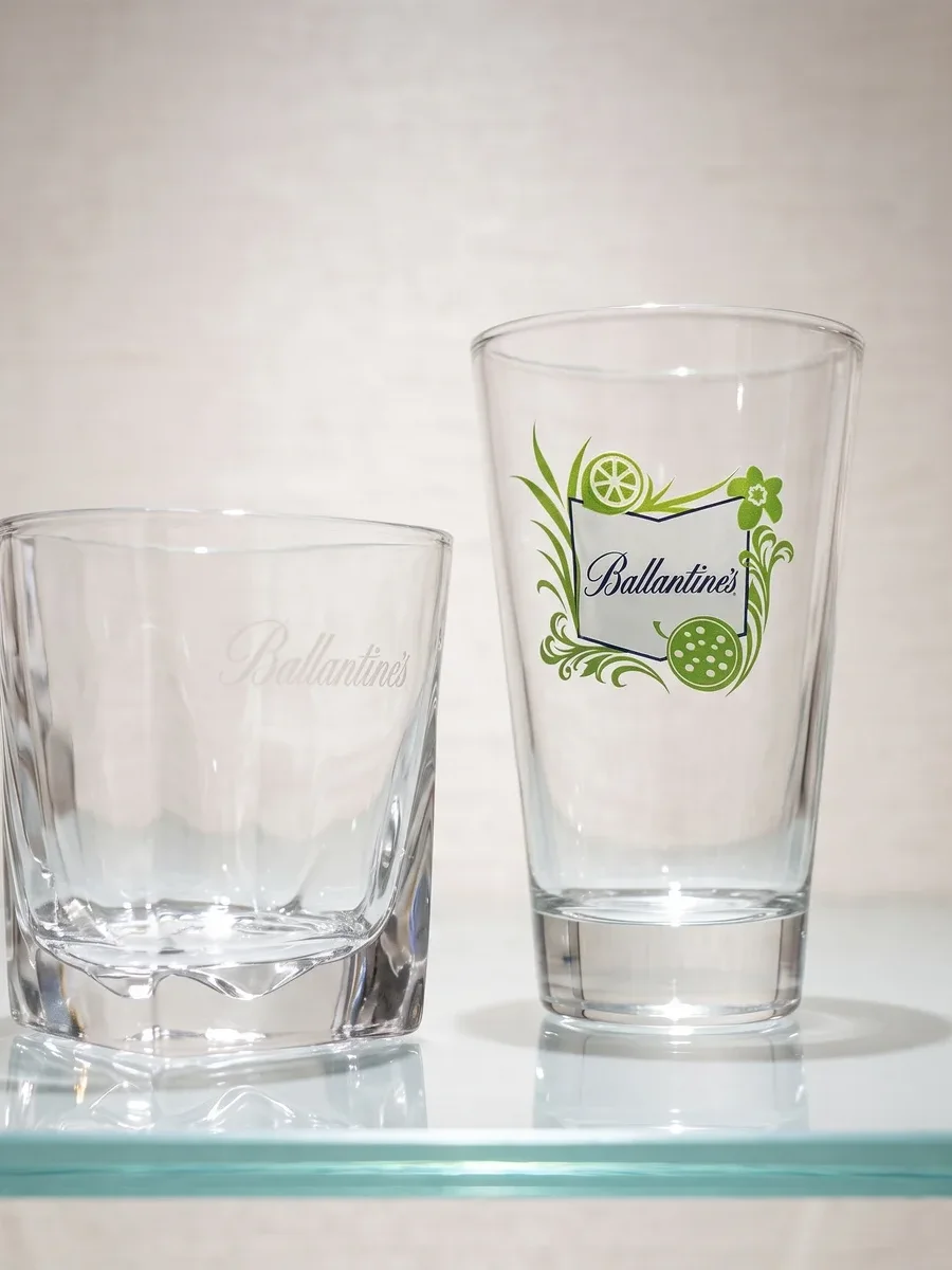 Vastag talpú whiskys és magas üdítős edény Ballantine's grafikával, napfényes teraszon