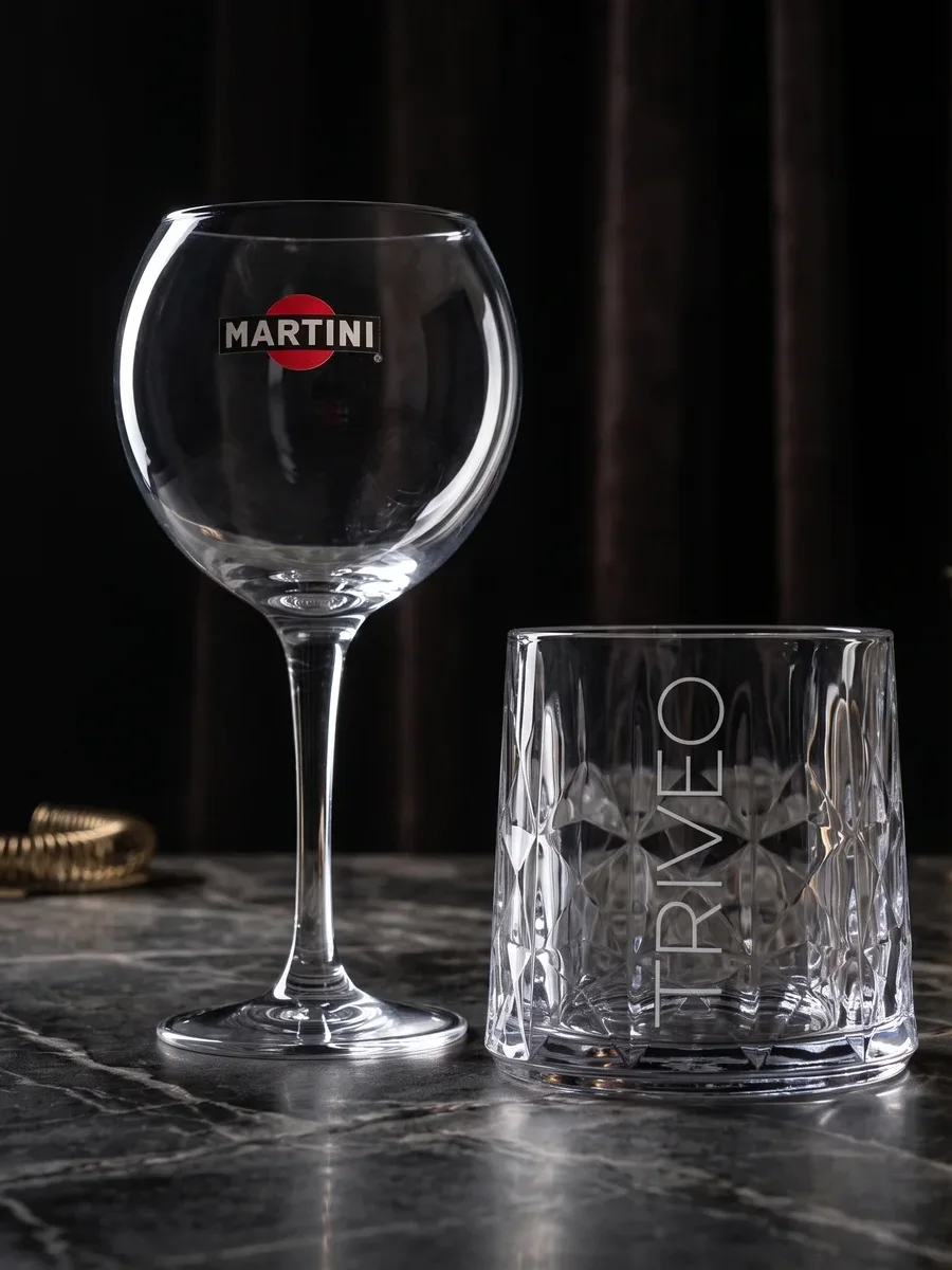 Martini talpas és csiszolt whiskys üvegedény sötét bárpulton, üvegespolc előtt