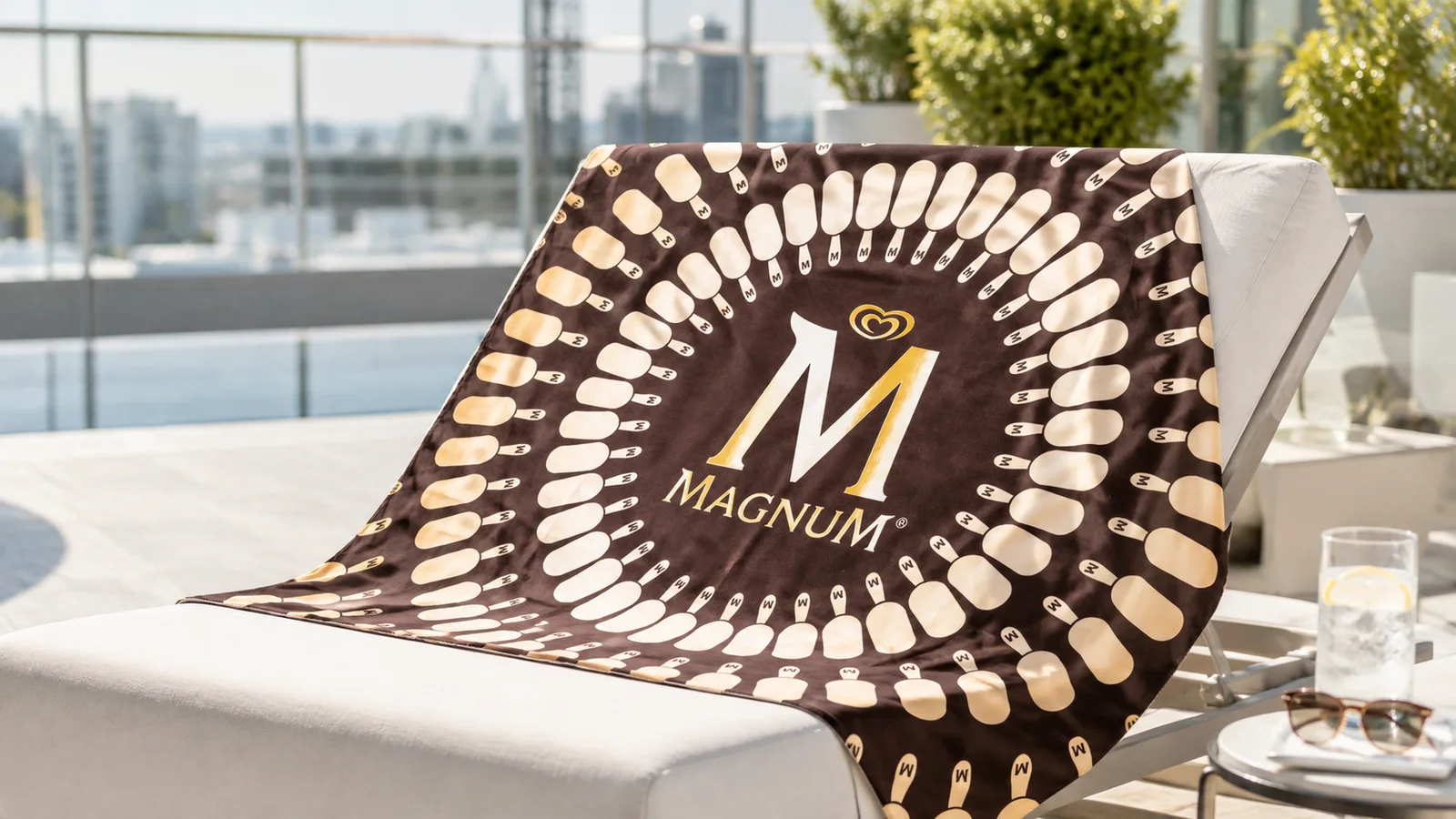 Barna-arany mintás frottír kendő Magnum emblémával, napozóágyon